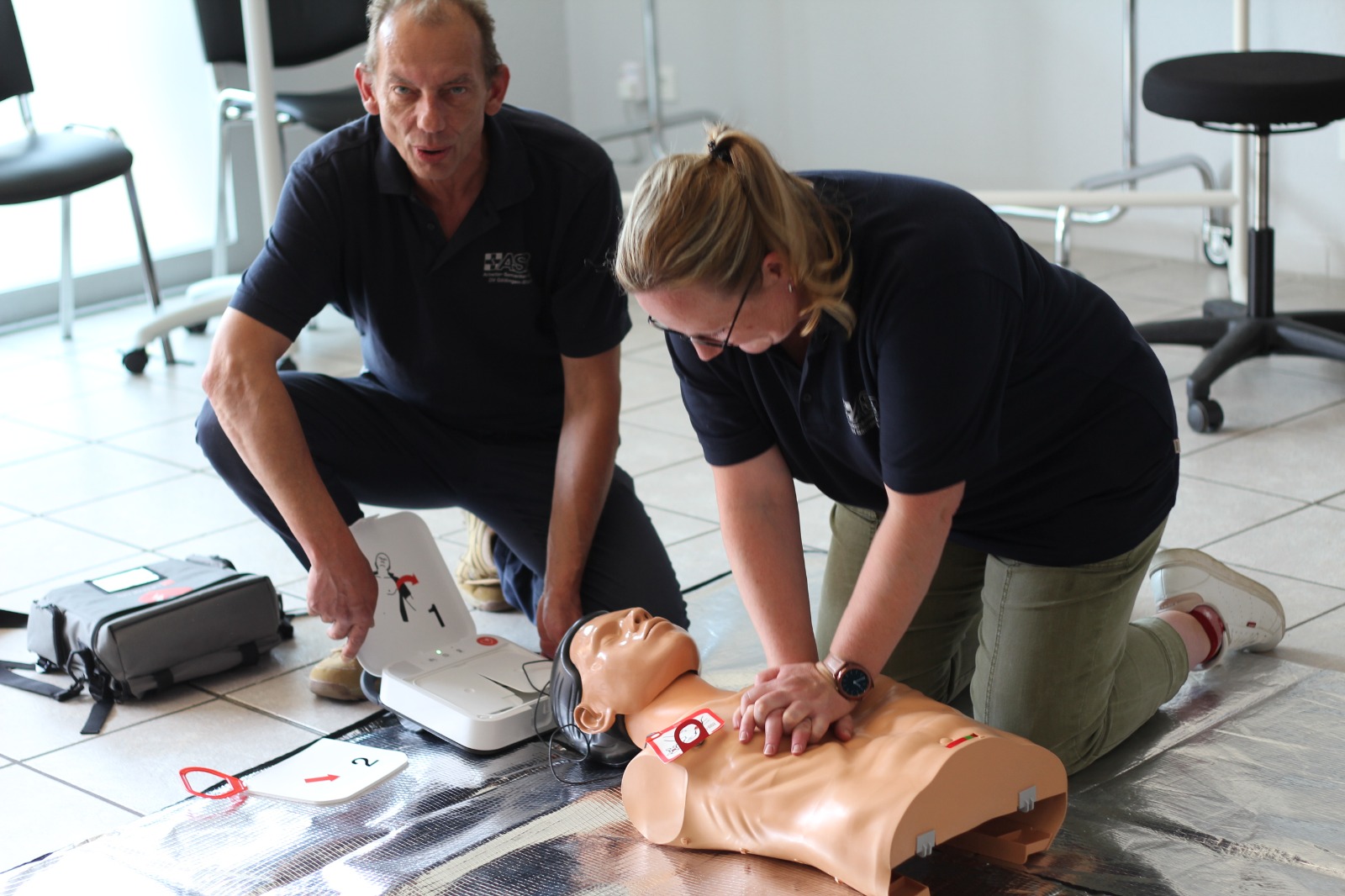 Auf dem Bild sind zwei Personen abgebildet, die an einer Puppe erste Hilfe leisten.