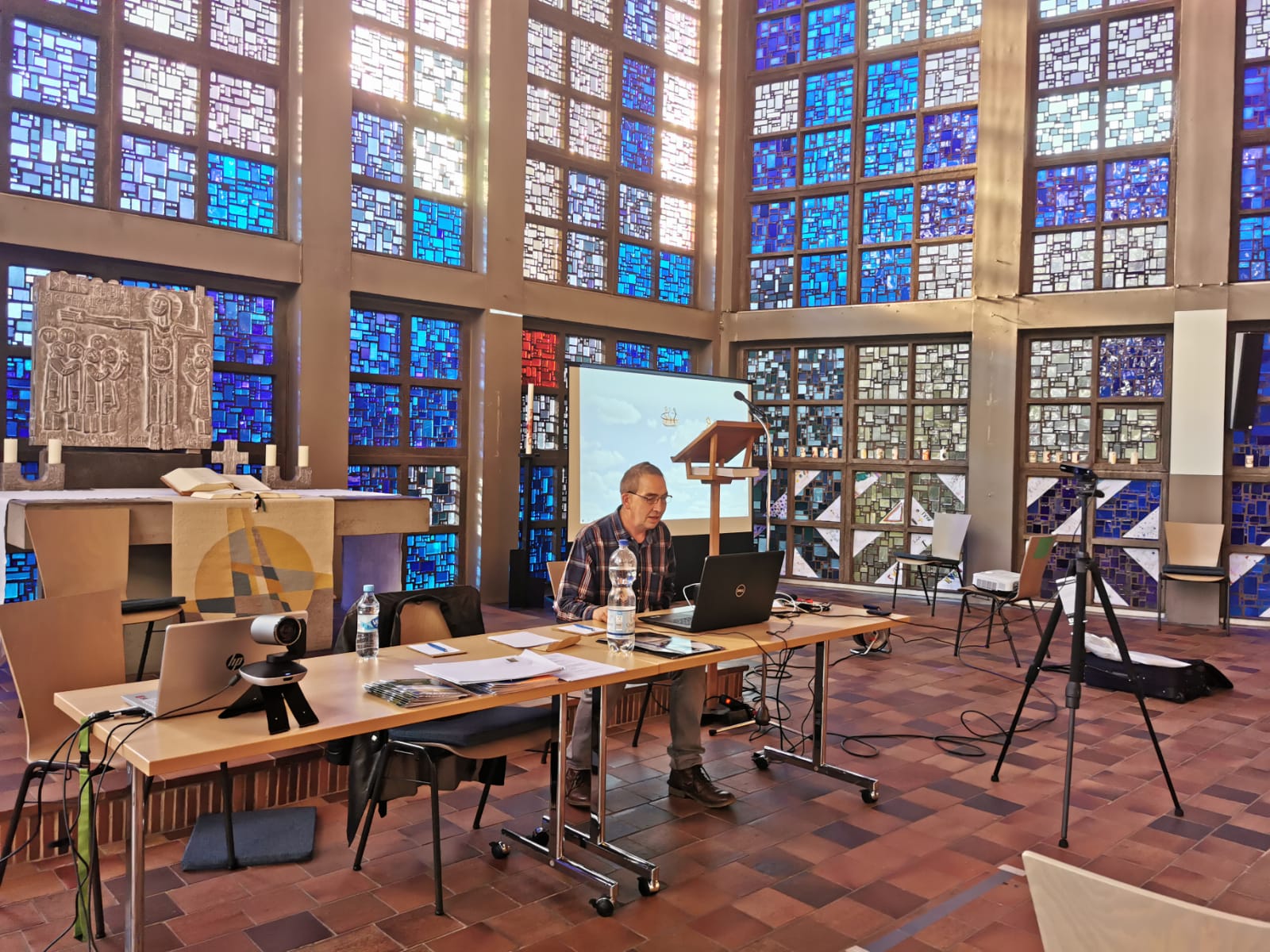 Mensch sitzt mit Technik für eine digitale Veranstaltung in einer Kirche vor Buntglasfenstern