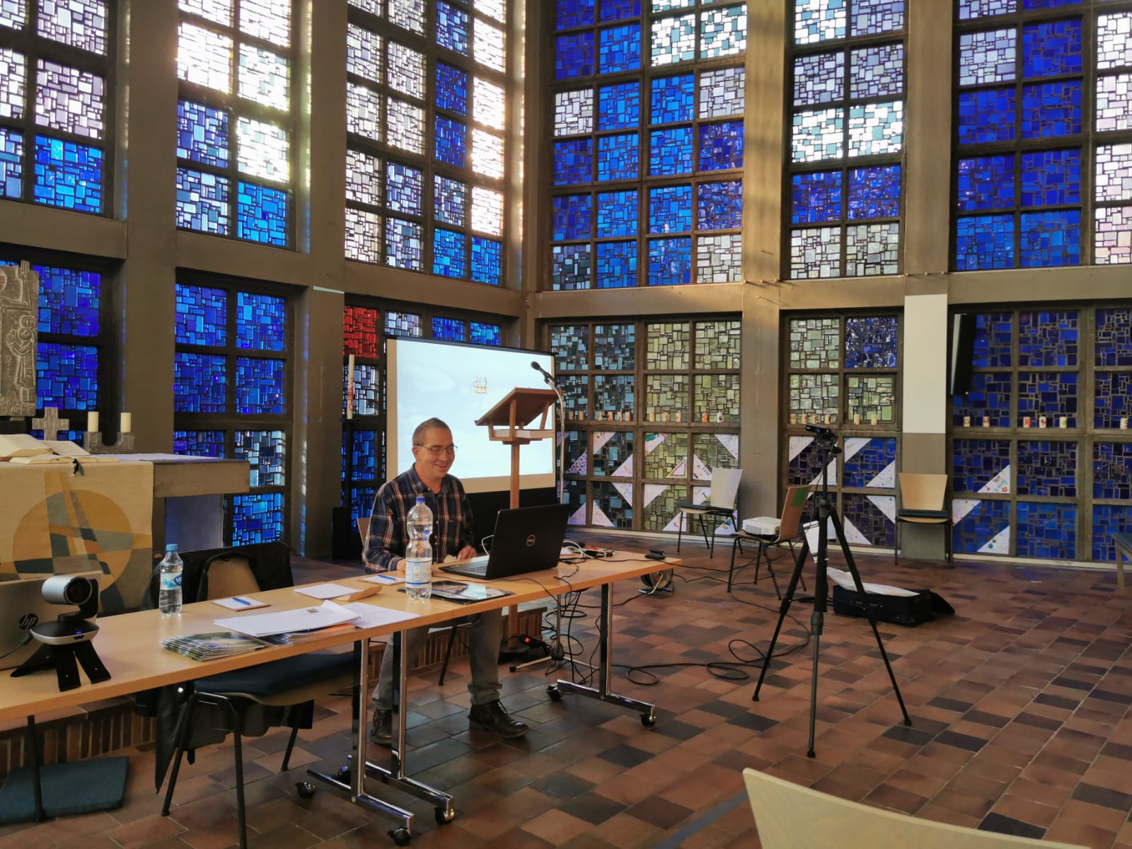 Mensch sitzt mit Technik für eine digitale Veranstaltung vor Buntglasfenstern einer Kirche