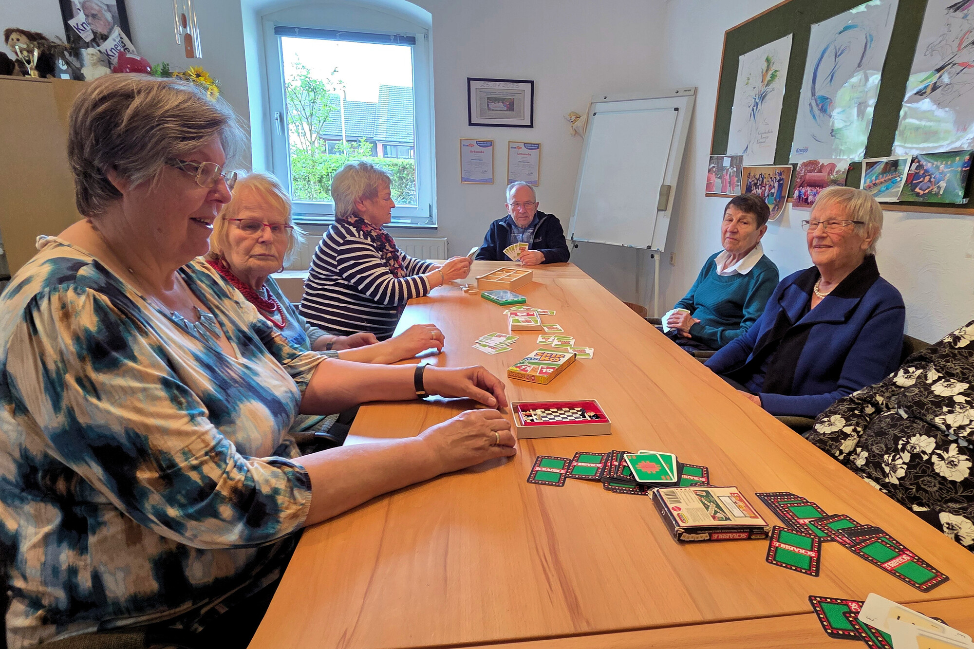 Das Bild zeigt mehrere Personen an einem Tisch sitzend und Karten spielen.