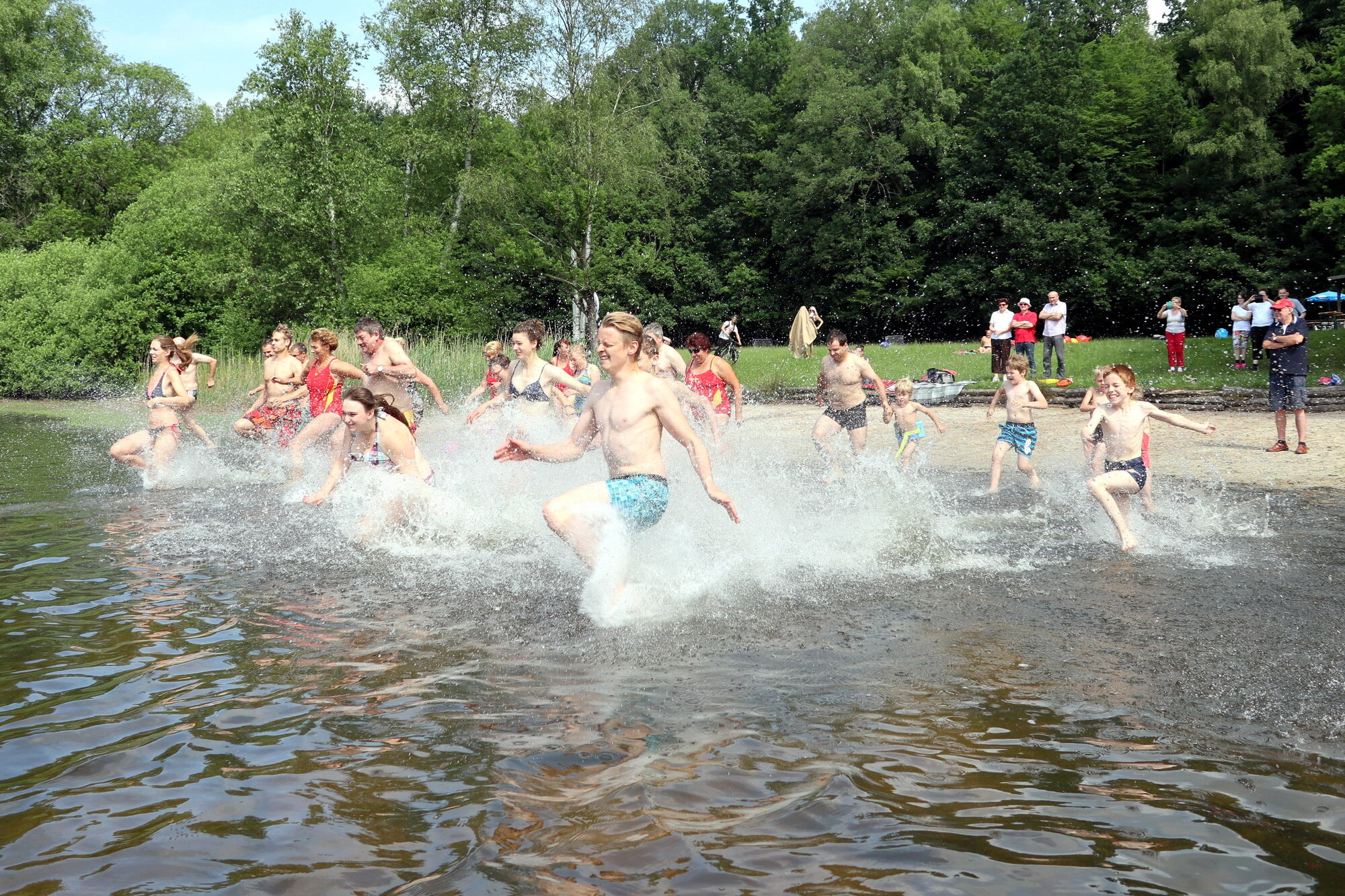 Menschen in Badekleidung stürmen gemeinsam in einen See