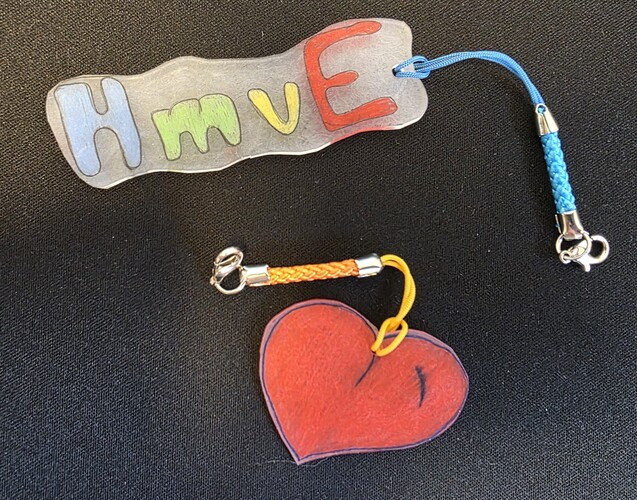 Das Bild zeigt zwei Schlüsselanhänger, einer mit rotem Herz, der zweite mit dem Schriftzug HmvE