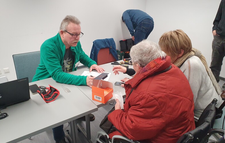Ein Reparateur des Repair-Cafés hilf zwei Frauen bei der Reparatur eines Elektrogerätes.