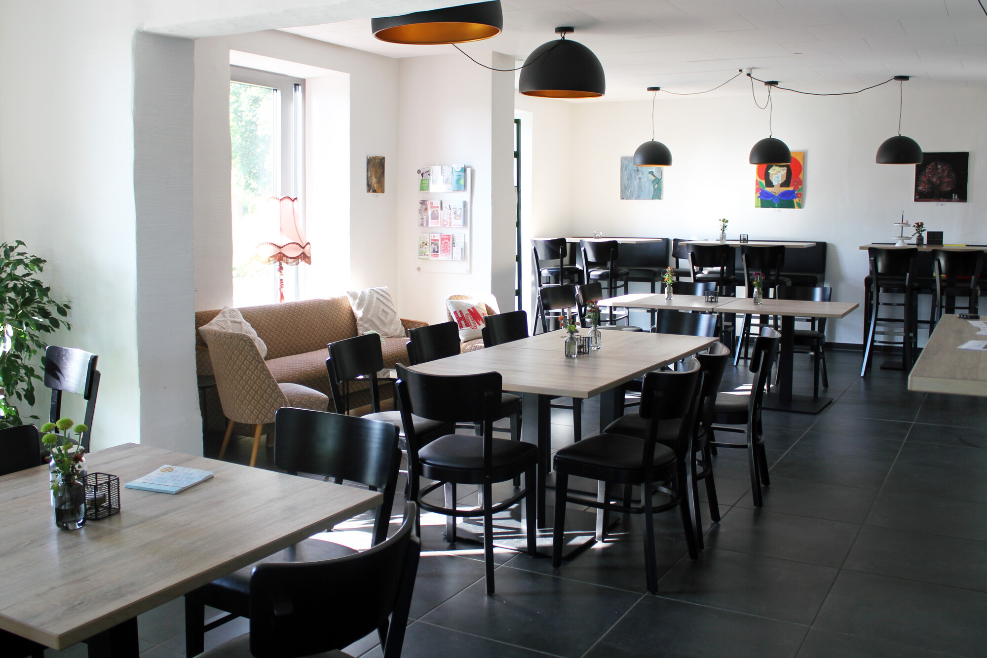 Das Bild zeigt mehrere Tische mit Stühlen und ein Sofa die im lichtdurchfluteten Raum stehen.